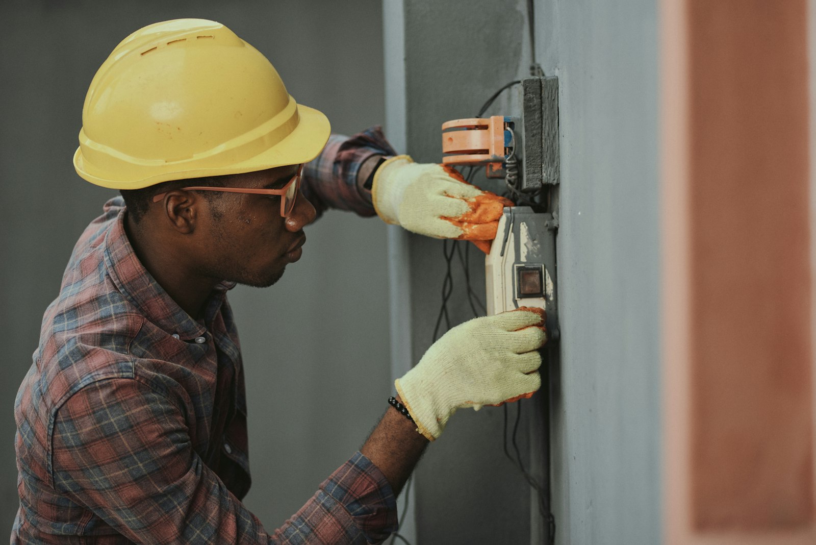 A TrueNorth technician in gloves and a hard hat working carefully on a wall-mounted control unit