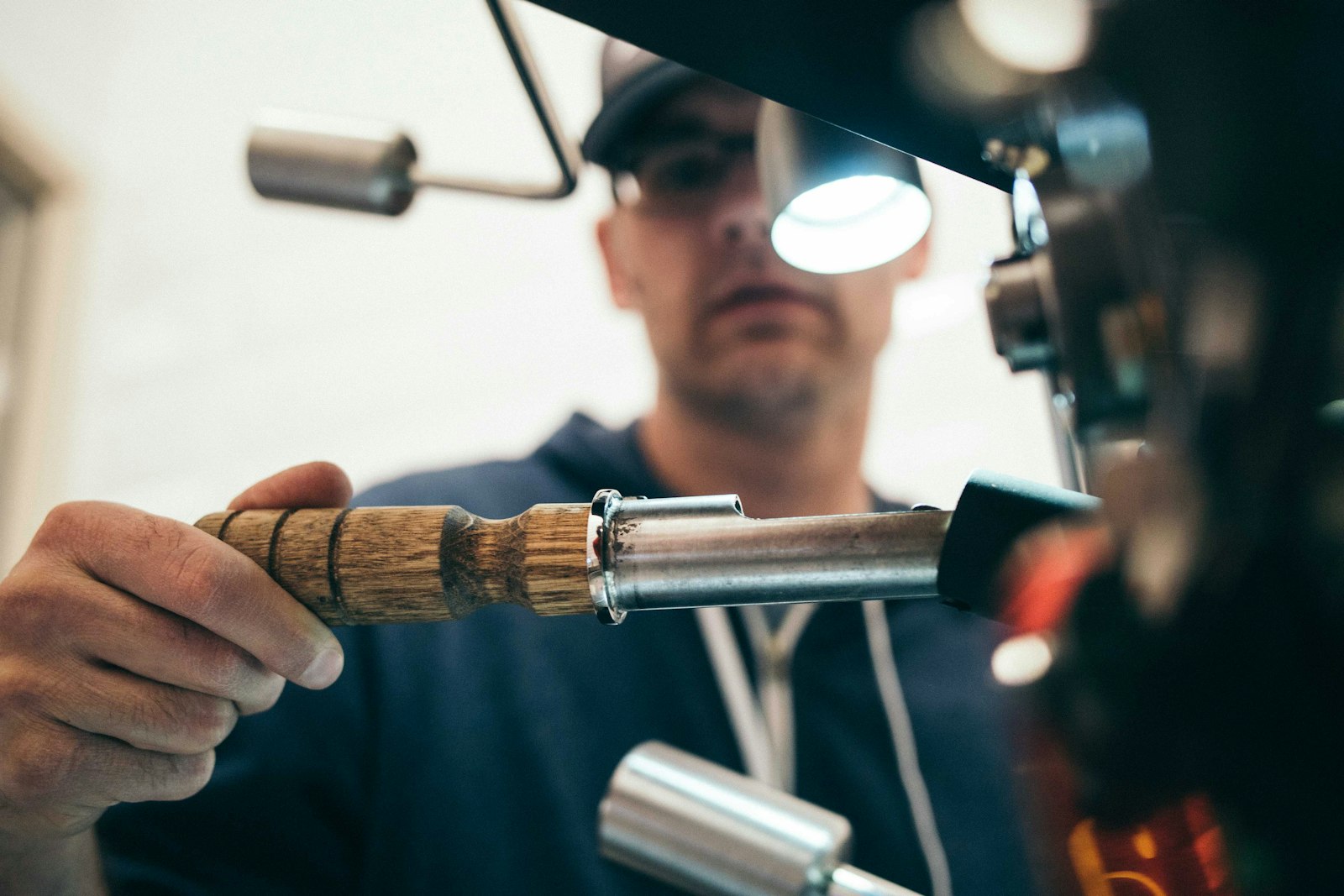 A technician in a workshop inspecting a hand tool under a work light, concentrating closely